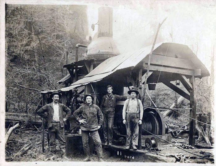 Four loggers in Portland Lumber Company camp posing with a steam donkey